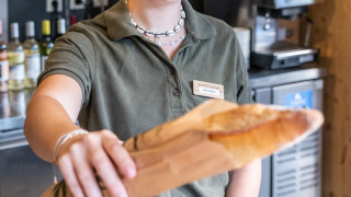 Empleada sonriente en Huttopia Oléron les Pins entrega una baguette en la panadería del parque vacacional.