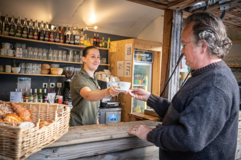 Un hombre recibe una taza de café de una empleada en una cafetería al aire libre en Huttopia Oléron les Pins, Francia.