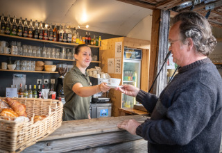 En mand får serveret en kop kaffe af en medarbejder i en udendørs café ved Huttopia Oléron les Pins, Frankrig.