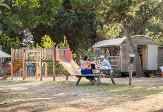 Udsigt over legeplads og picnicbord med mennesker ved Huttopia Oléron les Pins i Nouvelle-Aquitaine, Frankrig.