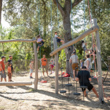 Kinderen en volwassenen klimmen en spelen op een buitenspeelplaats tussen de bomen bij Huttopia Oléron les Pins.