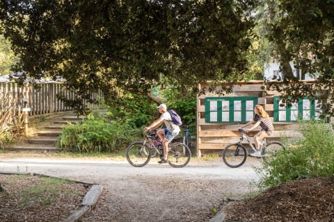 Dos personas montan en bicicleta por un camino sombreado en Huttopia Oléron les Pins, Francia.