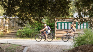 Dos personas montan en bicicleta por un camino sombreado en Huttopia Oléron les Pins, Francia.