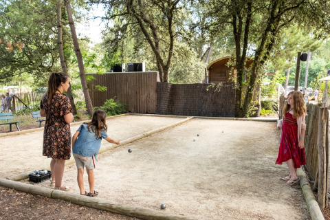 Niños y una adulta juegan a la petanca en una pista de grava en medio de árboles en Huttopia Oléron les Pins, Francia.