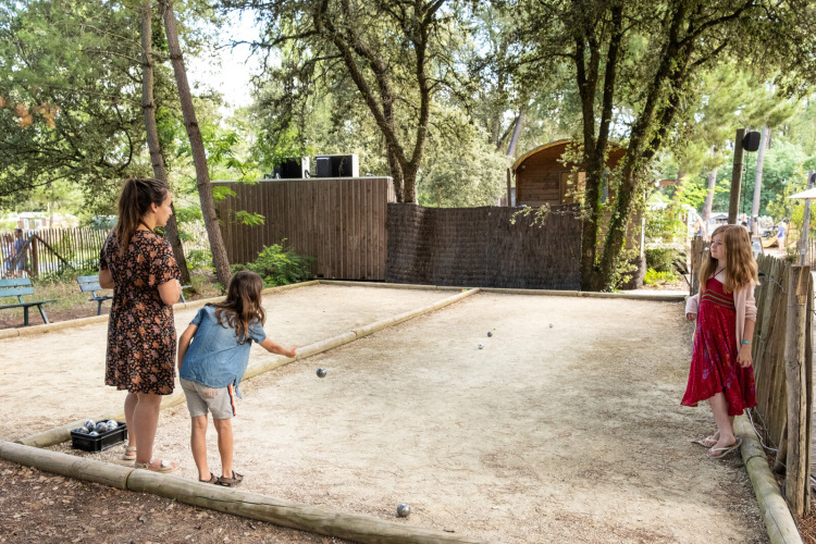 Kinderen en een volwassene spelen jeu de boules op een grindbaan in Huttopia Oléron les Pins, Frankrijk.