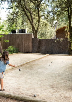 Niños y una adulta juegan a la petanca en una pista de grava en medio de árboles en Huttopia Oléron les Pins, Francia.