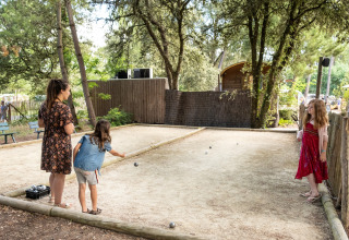 Bambini e un'adulta giocano a pétanque su un campo in ghiaia a Huttopia Oléron les Pins, Francia.