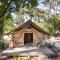 Trapper safari-tent met houten terras, twee stoelen en fiets, omringd door bomen in de zon.