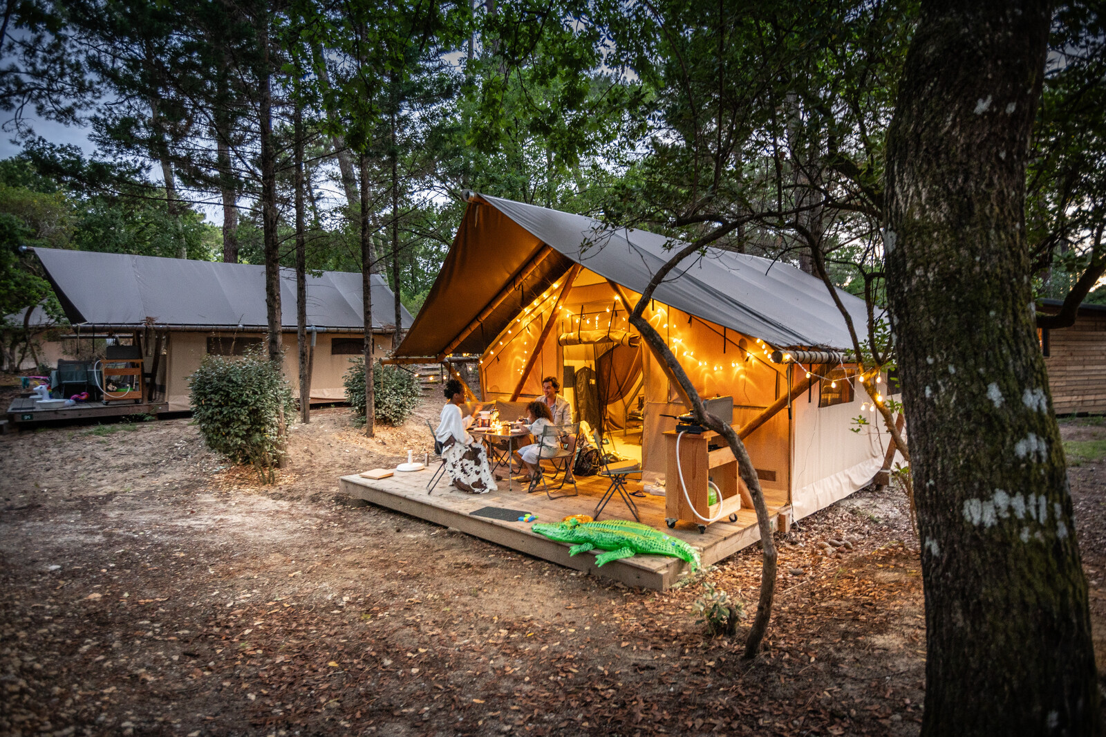 Gezin dineert buiten bij verlichte Trapper safaritent in Huttopia Arcachon, Frankrijk, in het bos.