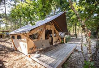 Tienda safari Trapper en Huttopia Arcachon, Francia, rodeada de árboles y naturaleza con terraza de madera.