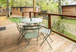 Udendørs træterrasse med bord og stole ved Chalet Evasion, Huttopia Arcachon, omgivet af skov og hytter.