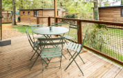 Terrazza in legno con tavolo e sedie presso Chalet Evasion, Huttopia Arcachon, circondata da alberi e chalet.