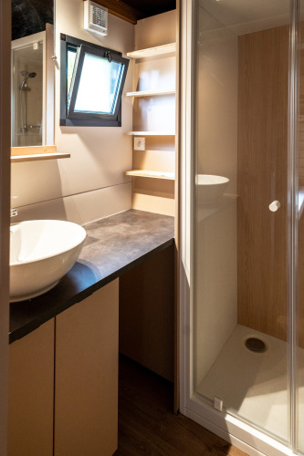 Bagno moderno nello Chalet Evasion a Huttopia Arcachon, Francia, con cabina doccia, lavabo a ciotola e finestra aperta.