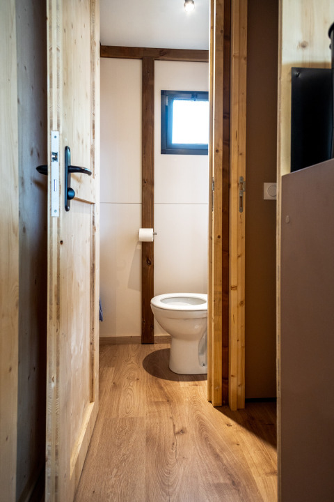 Foto di un semplice bagno con pavimento in legno e WC nello Chalet Evasion presso Huttopia Arcachon, Francia.
