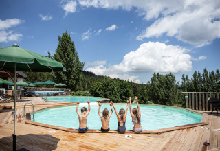 Bambini seduti a bordo piscina a Huttopia Font-Romeu, parco vacanze in Occitania, Francia, circondati dalla natura.