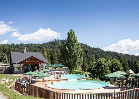 Piscina al aire libre con sombrillas verdes entre colinas boscosas en Huttopia Font-Romeu, Occitanie, Francia.