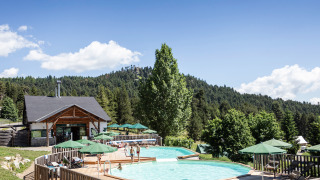 Piscina al aire libre con sombrillas verdes entre colinas boscosas en Huttopia Font-Romeu, Occitanie, Francia.