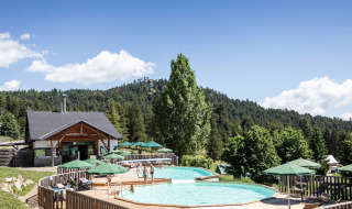 Piscina al aire libre con sombrillas verdes entre colinas boscosas en Huttopia Font-Romeu, Occitanie, Francia.