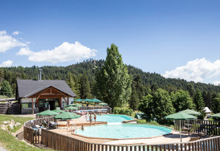 Piscina al aire libre con sombrillas verdes entre colinas boscosas en Huttopia Font-Romeu, Occitanie, Francia.