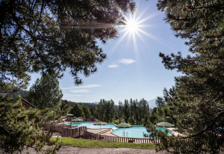 Door de bomen zicht op het zwembad van Huttopia Font-Romeu vakantiepark in Occitanië, Frankrijk op een zonnige dag.