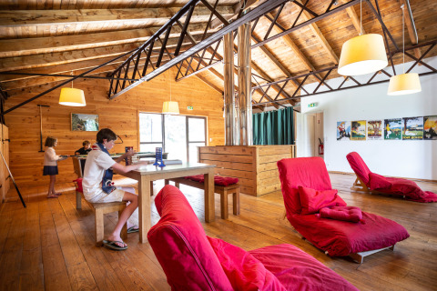 Sala de estar de madera con niños jugando y sillones rojos en Huttopia Font-Romeu, Occitanie, Francia.