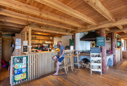 Houten bar met bezoekers en barman bij Huttopia Font-Romeu vakantiepark in Occitanië, Frankrijk.