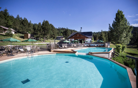 Außenpool mit Liegen und Sonnenschirmen im Ferienpark Huttopia Font-Romeu in Okzitanien, Frankreich.