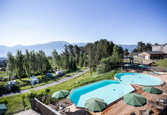Udsigt over pools og campingvogne omringet af træer på Huttopia Font-Romeu feriepark i Occitanie, Frankrig