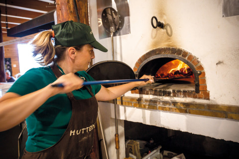 Mujer horneando pizza en horno de leña en Huttopia Font-Romeu, parque vacacional en Occitania, Francia.