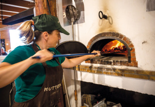 Vrouw bakt pizza in een traditionele houtoven bij Huttopia Font-Romeu vakantiepark in Occitanië, Frankrijk.