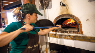 Mujer horneando pizza en horno de leña en Huttopia Font-Romeu, parque vacacional en Occitania, Francia.