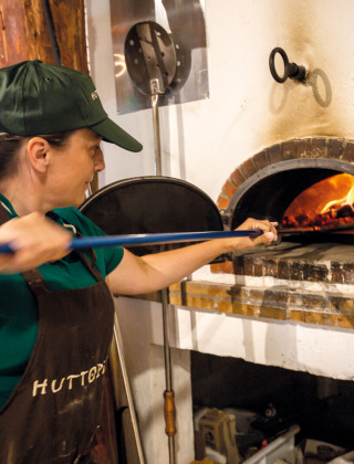 Mujer horneando pizza en horno de leña en Huttopia Font-Romeu, parque vacacional en Occitania, Francia.