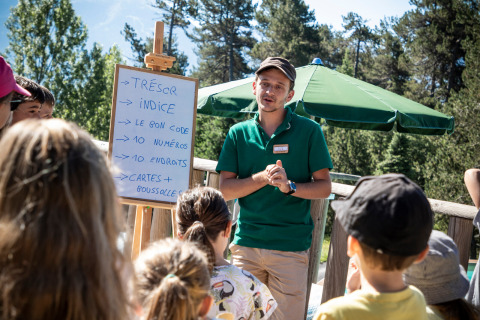 Monitor explicando reglas de búsqueda del tesoro a niños al aire libre en Huttopia Font-Romeu, Occitania, Francia.