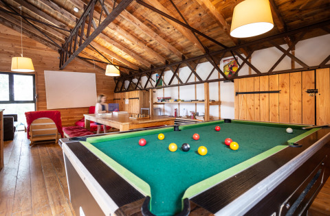 Sala de juegos con mesa de billar, paredes de madera e iluminación cálida en Huttopia Font-Romeu, Occitania, Francia.