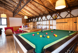 Spelruimte met pooltafel, houten muren en warme verlichting in Huttopia Font-Romeu, Occitanië, Frankrijk.