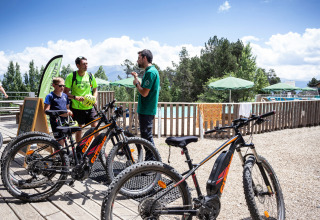 Menschen unterhalten sich neben E-Mountainbikes im Ferienpark Huttopia Font-Romeu in Occitanie, Frankreich.