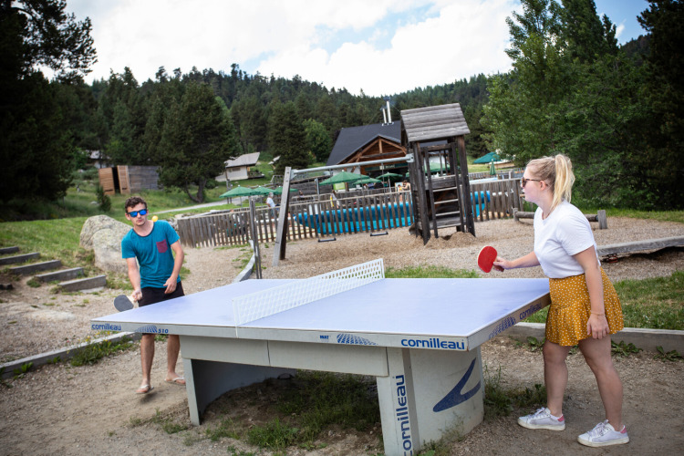 Zwei Menschen spielen Tischtennis im Freien im Ferienpark Huttopia Font-Romeu in Okzitanien, Frankreich.