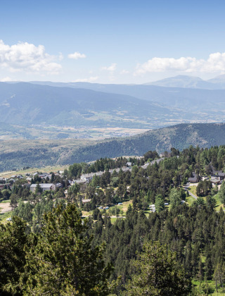 Vista de colinas verdes, casas y bosques cerca de Font-Romeu en Occitania, Francia, con montañas al fondo.