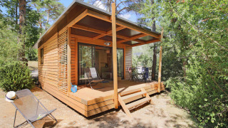 Chalet Victoria de madera, con terraza cubierta y sillas, rodeado de bosques y naturaleza tranquila.