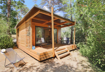 Chalet Victoria, houten chalet met overdekt terras en stoelen, gelegen in een rustige, groene omgeving.