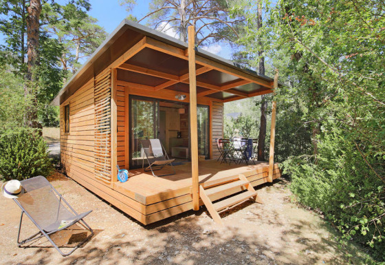 Chalet Victoria de madera, con terraza cubierta y sillas, rodeado de bosques y naturaleza tranquila.