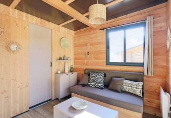 LICHT HOUTEN INTERIEUR VAN CHALET VICTORIA MET BANK EN GROTE RAAM BIJ HUTTOPIA ARCACHON, FRANKRIJK.