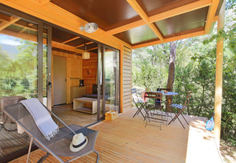 Holzterrasse mit Liegestuhl und Tisch am Chalet Victoria im Huttopia Arcachon, umgeben von grüner Natur in Frankreich.