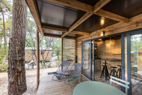Træterrasse med stole og bord ved Chalet Victoria, Huttopia Arcachon, omgivet af skov i Frankrig.