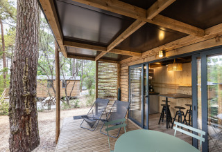 Houten terras met stoelen bij Chalet Victoria, Huttopia Arcachon, Frankrijk, omringd door bos.