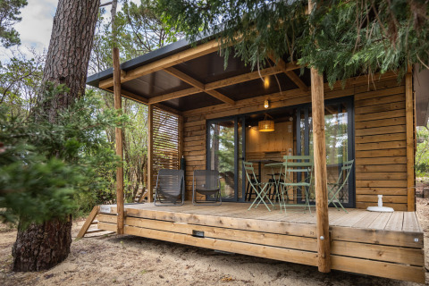 Vista exterior del Chalet Victoria en Huttopia Arcachon, Francia, con terraza de madera y muebles de jardín.