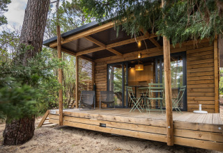 Vista exterior del Chalet Victoria en Huttopia Arcachon, Francia, con terraza de madera y muebles de jardín.