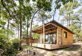 Træchalet Victoria ved Huttopia Arcachon i Frankrig, omgivet af grønne træer og natur, afslappende atmosfære