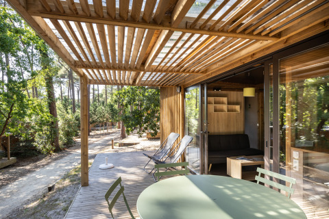 Solrige terrasse og moderne interiør i Chalet Portland, Huttopia Arcachon, omgivet af smuk skov i Frankrig.