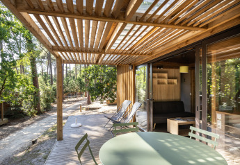 Solrige terrasse og moderne interiør i Chalet Portland, Huttopia Arcachon, omgivet af smuk skov i Frankrig.
